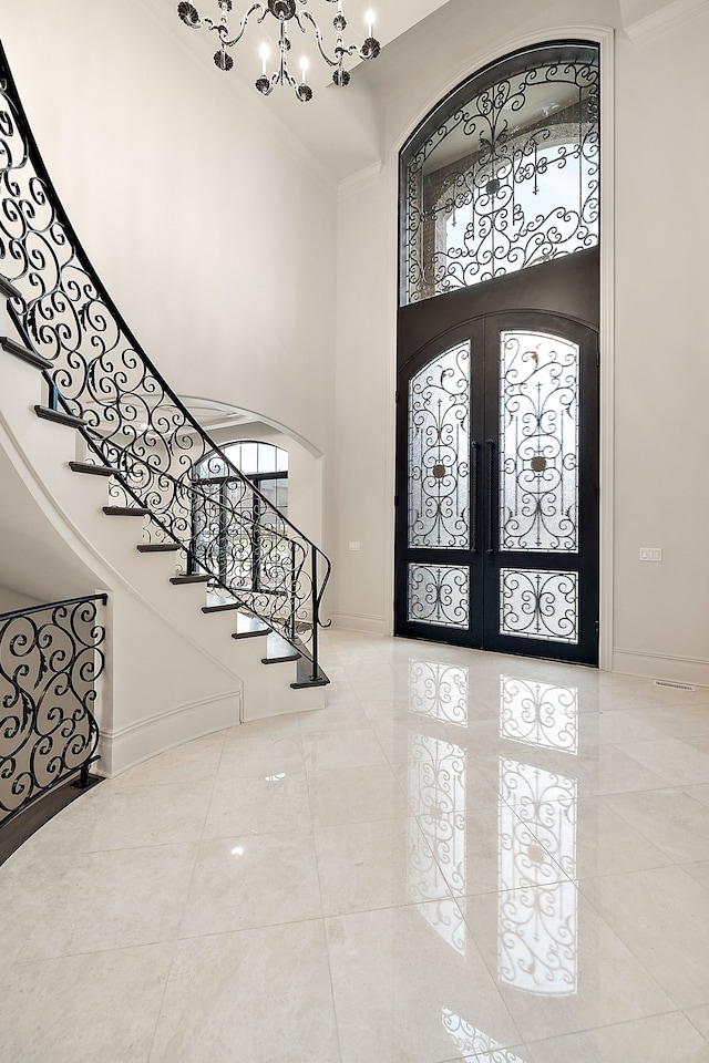 entryway featuring crown molding, french doors, a towering ceiling, and an inviting chandelier