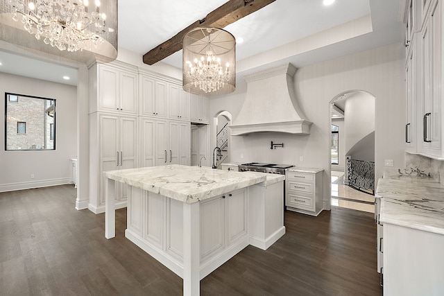 kitchen featuring beamed ceiling, decorative light fixtures, a center island with sink, white cabinets, and custom exhaust hood