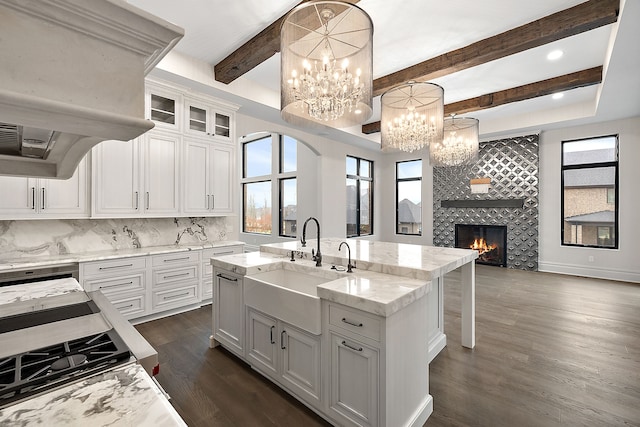 kitchen featuring white cabinets, pendant lighting, a kitchen island with sink, and a tiled fireplace