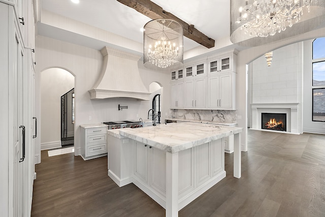 kitchen featuring premium range hood, an island with sink, beamed ceiling, dark hardwood / wood-style flooring, and white cabinetry