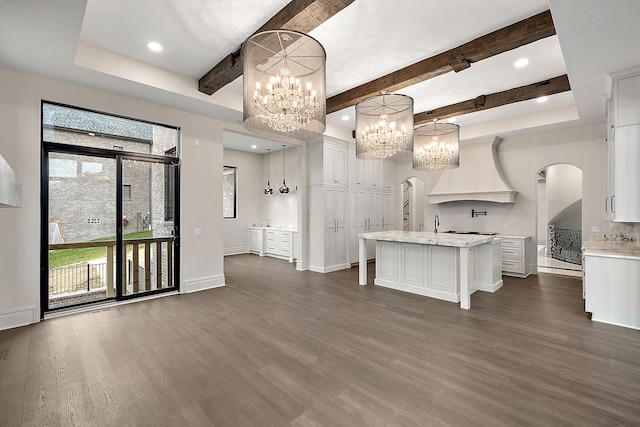 kitchen with beam ceiling, dark wood-type flooring, hanging light fixtures, a center island with sink, and white cabinets