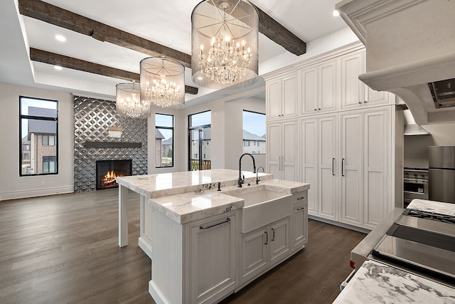 kitchen with sink, decorative light fixtures, a tiled fireplace, white cabinetry, and an island with sink