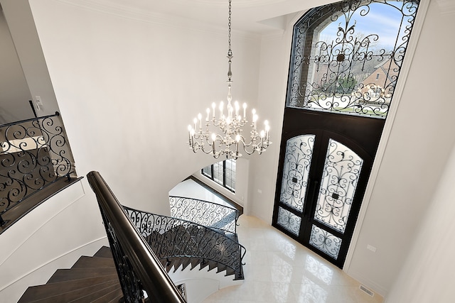 foyer featuring a chandelier, french doors, a towering ceiling, and ornamental molding