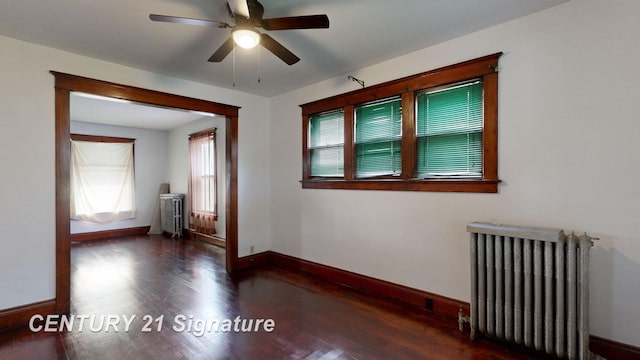 spare room with dark wood-type flooring, ceiling fan, and radiator