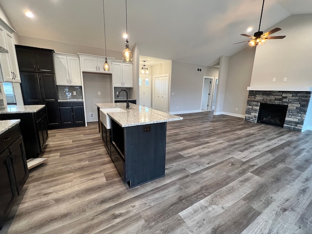 kitchen featuring tasteful backsplash, light stone counters, open floor plan, a stone fireplace, and a sink