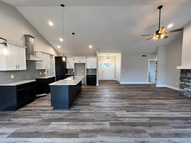 kitchen with an island with sink, ceiling fan, wall chimney exhaust hood, and open floor plan