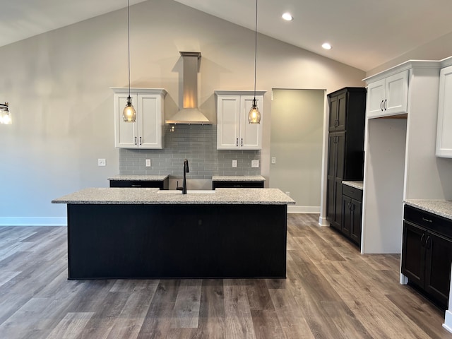 kitchen with wood finished floors, a sink, backsplash, wall chimney exhaust hood, and pendant lighting