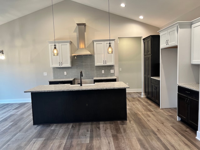 kitchen with wood finished floors, a sink, vaulted ceiling, wall chimney range hood, and decorative backsplash