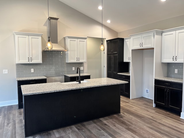 kitchen featuring wood finished floors, wall chimney range hood, a sink, and a kitchen island with sink