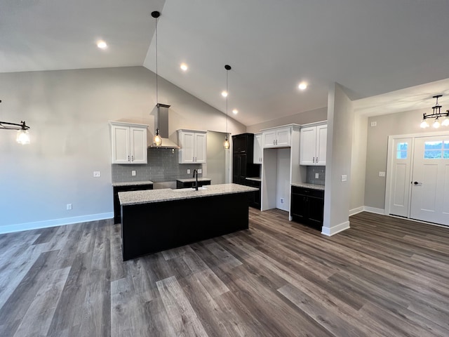 kitchen with decorative backsplash, dark wood-type flooring, a kitchen island with sink, a sink, and wall chimney range hood