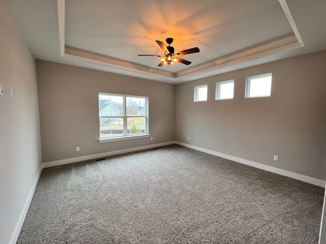 carpeted spare room with a ceiling fan, a tray ceiling, visible vents, and baseboards