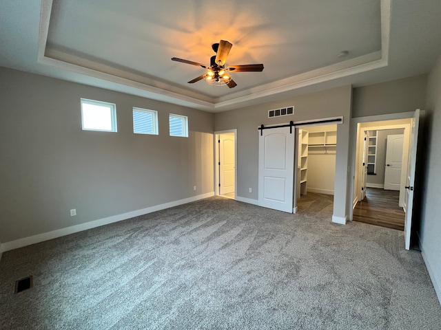 unfurnished bedroom with a tray ceiling, a barn door, and visible vents