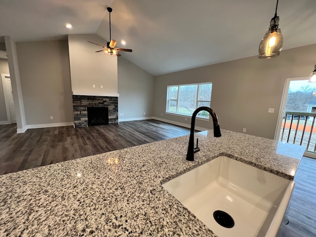 kitchen with wood finished floors, light stone countertops, vaulted ceiling, a fireplace, and a sink