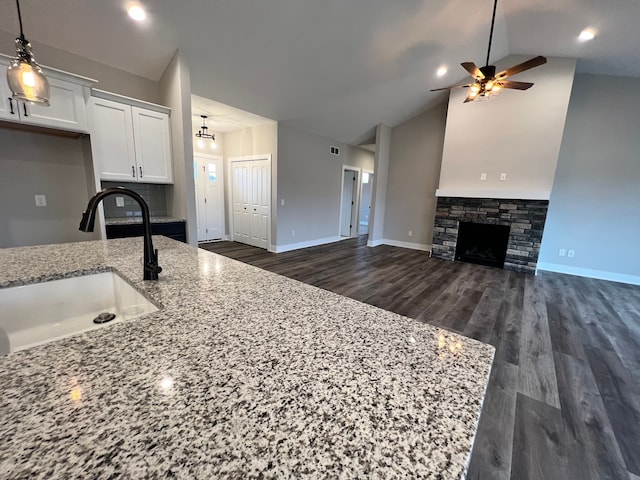 kitchen featuring a stone fireplace, a sink, white cabinets, open floor plan, and light stone countertops