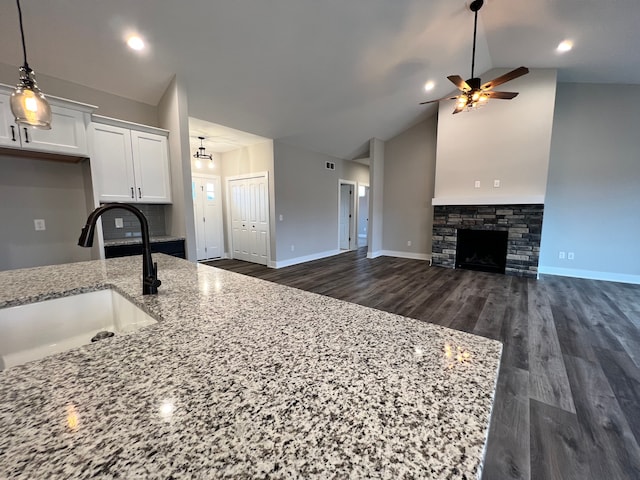 kitchen featuring light stone counters, a fireplace, a sink, white cabinetry, and open floor plan