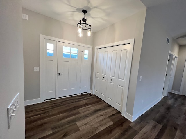 foyer with dark wood-type flooring, an inviting chandelier, visible vents, and baseboards