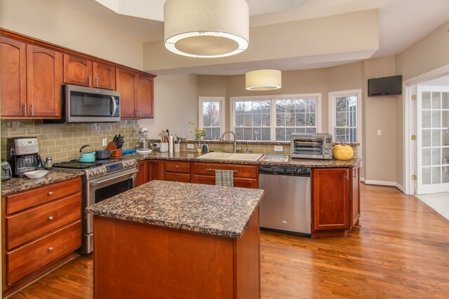 kitchen featuring sink, dark stone countertops, appliances with stainless steel finishes, light hardwood / wood-style floors, and kitchen peninsula