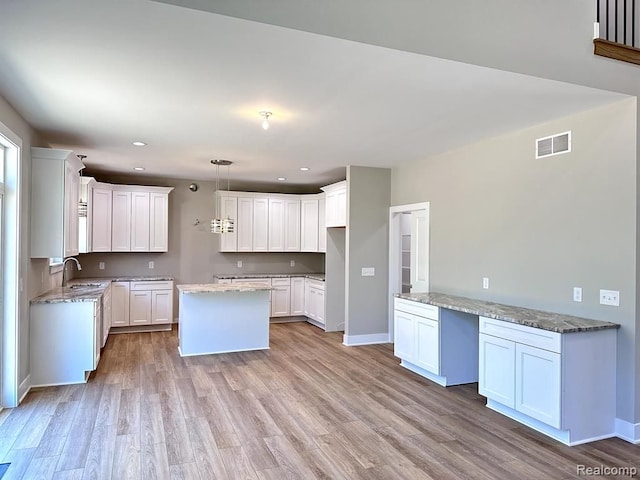 kitchen featuring light stone counters, sink, decorative light fixtures, white cabinets, and light hardwood / wood-style floors