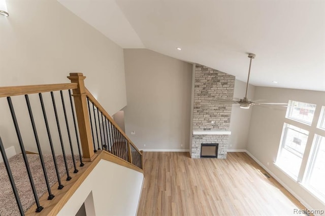 unfurnished living room with a stone fireplace, ceiling fan, lofted ceiling, and light wood-type flooring