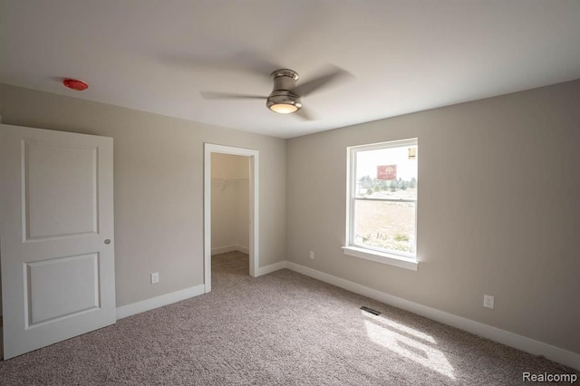 unfurnished bedroom with carpet flooring, a walk in closet, a closet, and ceiling fan