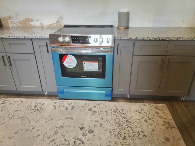 kitchen featuring light stone countertops, gray cabinets, dark hardwood / wood-style floors, and stainless steel electric range oven