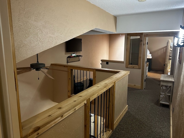 hall featuring a textured ceiling and dark colored carpet