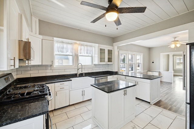 kitchen featuring decorative backsplash, appliances with stainless steel finishes, a kitchen island, dark stone countertops, and white cabinetry