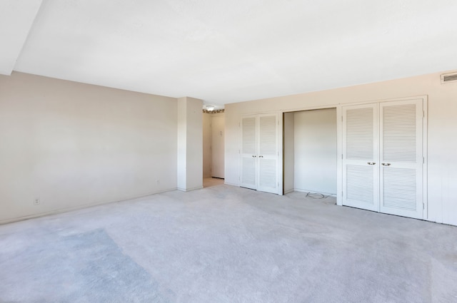 unfurnished bedroom featuring a notable chandelier, light carpet, and multiple closets