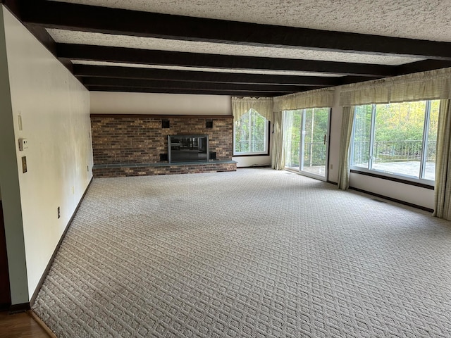 unfurnished living room with a fireplace, beam ceiling, carpet floors, and a textured ceiling