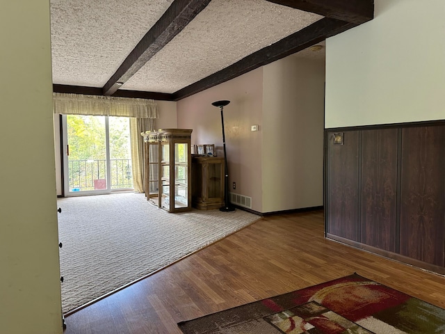 empty room with beam ceiling, wood-type flooring, a textured ceiling, and wooden walls