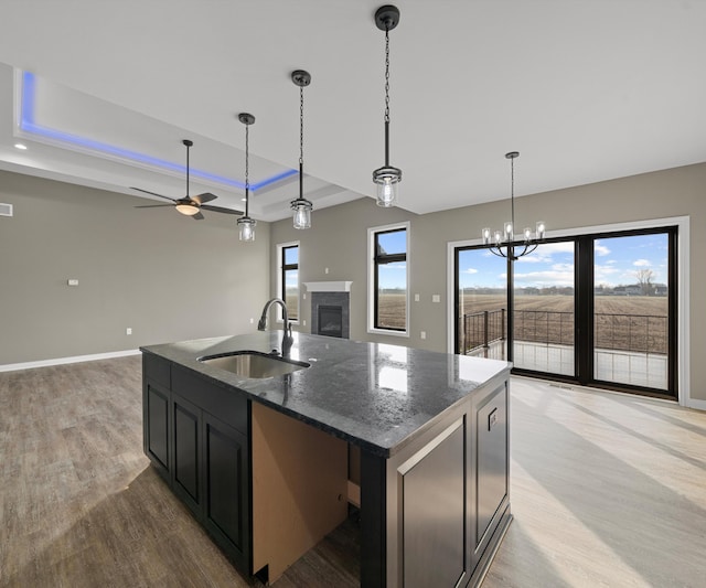 kitchen with a tray ceiling, a fireplace, open floor plan, a sink, and light wood-type flooring