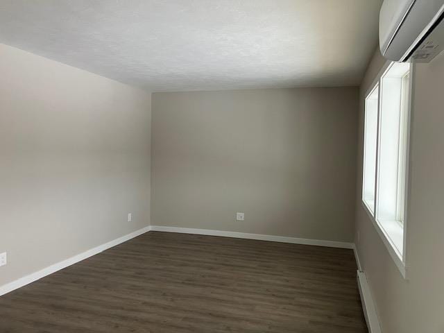 2715 Sawyer Rd, Traverse City, MI 49685 - spare room with a wall unit AC, dark wood-style floors, baseboards, and a textured ceiling