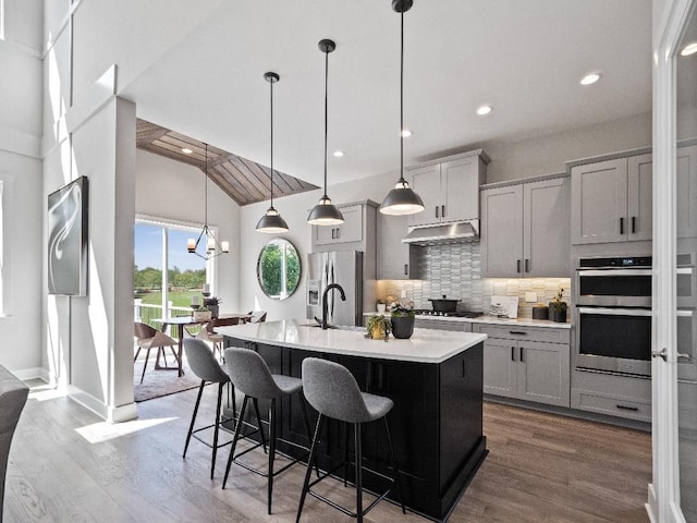 kitchen with hardwood / wood-style floors, gray cabinets, hanging light fixtures, and a kitchen island with sink