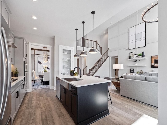 kitchen with appliances with stainless steel finishes, sink, pendant lighting, a center island with sink, and hardwood / wood-style floors