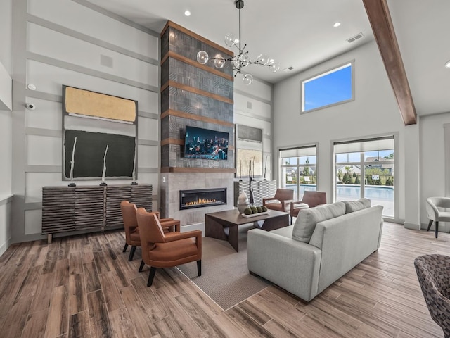 living room featuring a high ceiling, an inviting chandelier, a fireplace, beam ceiling, and wood-type flooring