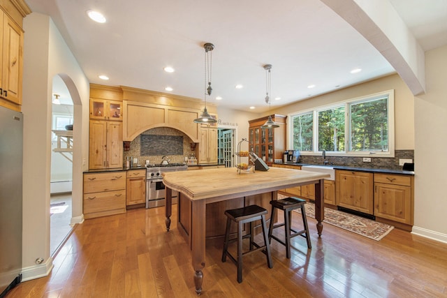 kitchen with pendant lighting, a center island with sink, wood-type flooring, butcher block counters, and stainless steel appliances