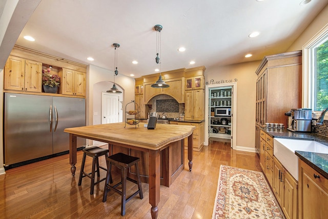 kitchen with a breakfast bar, backsplash, decorative light fixtures, light hardwood / wood-style floors, and stainless steel appliances