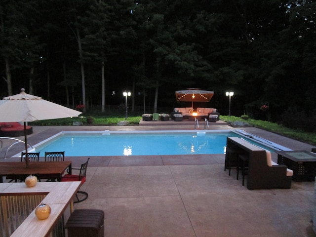 pool at twilight featuring a diving board and a patio