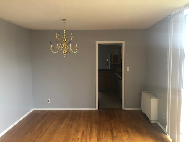 empty room featuring radiator, a chandelier, and dark wood-type flooring