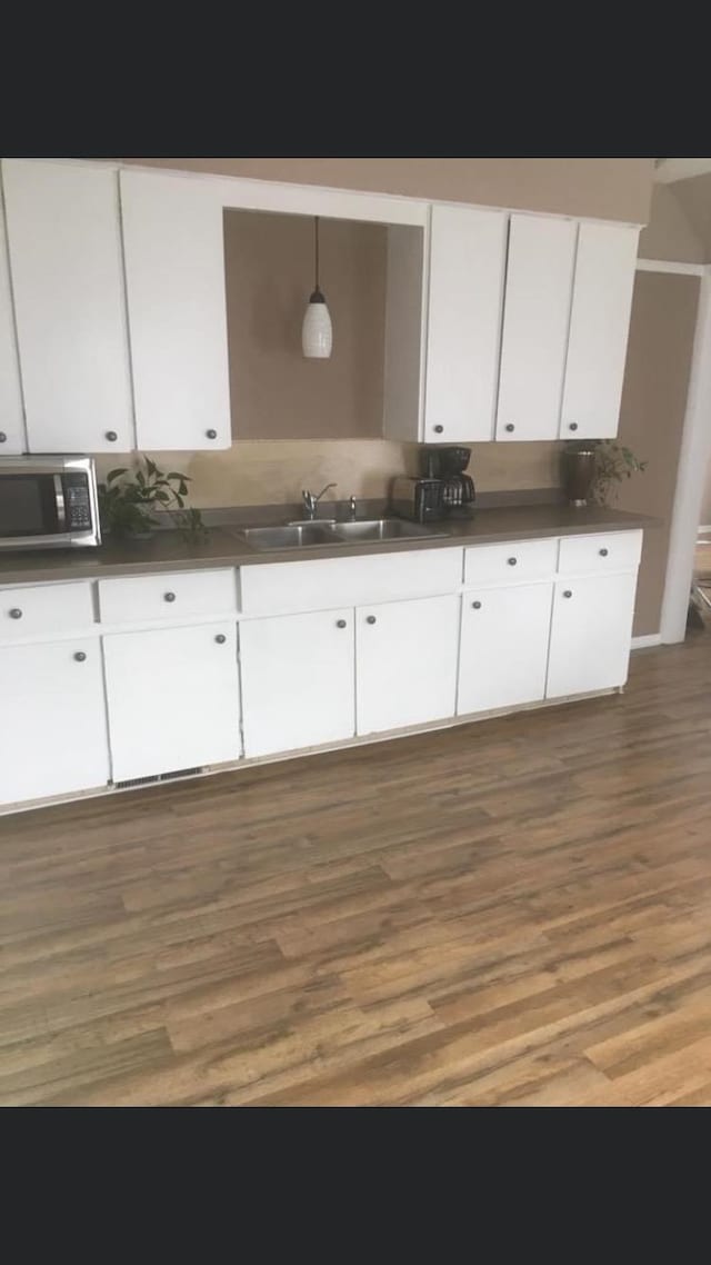 kitchen with white cabinetry, dark wood-type flooring, hanging light fixtures, and sink