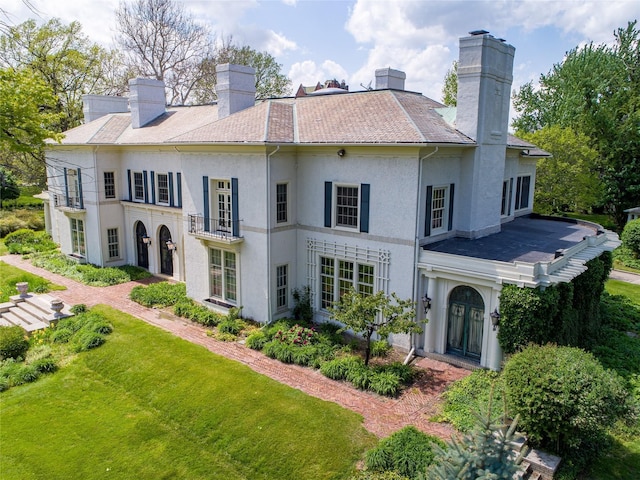 back of property with french doors, a yard, and a balcony