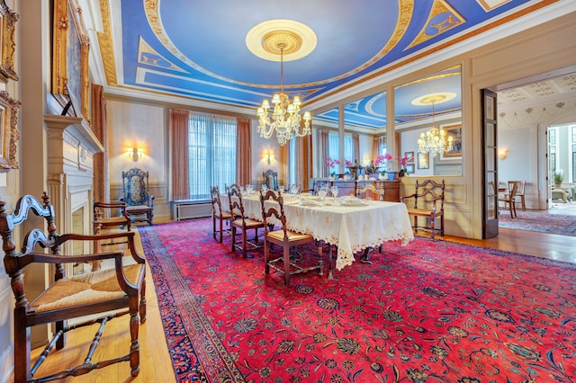 dining room with a raised ceiling, a premium fireplace, a notable chandelier, and ornamental molding