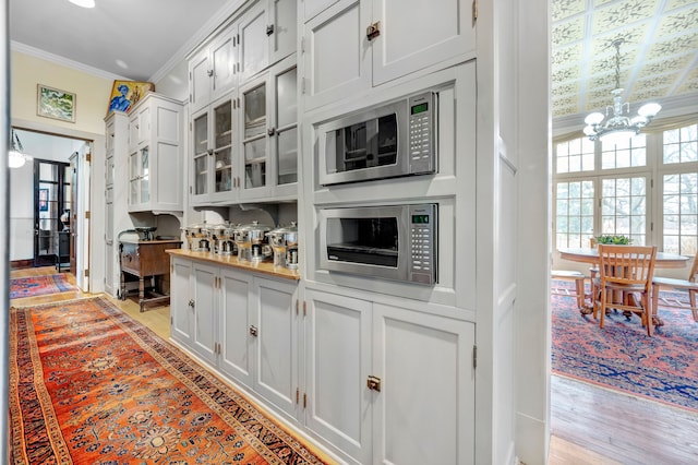 kitchen featuring crown molding, light hardwood / wood-style flooring, a notable chandelier, white cabinets, and stainless steel microwave