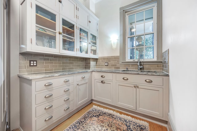 kitchen featuring backsplash, sink, light hardwood / wood-style floors, light stone counters, and white cabinetry