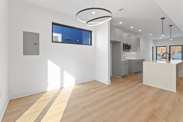 kitchen with gray cabinets, a kitchen island with sink, hanging light fixtures, and electric panel