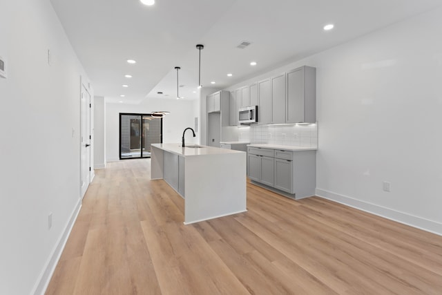 kitchen with backsplash, sink, gray cabinets, an island with sink, and light hardwood / wood-style floors