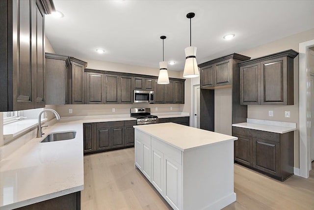 kitchen featuring sink, light wood-type flooring, appliances with stainless steel finishes, decorative light fixtures, and a kitchen island