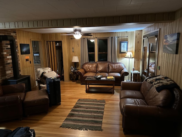 living room featuring ceiling fan, wood walls, a wood stove, and light hardwood / wood-style flooring