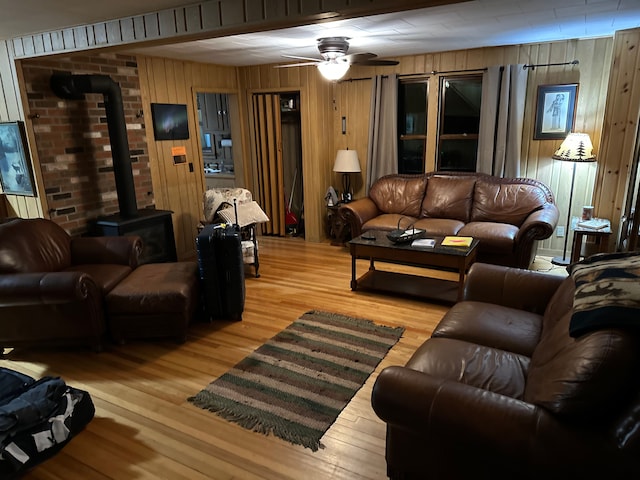 living room with light hardwood / wood-style floors, a wood stove, ceiling fan, and wooden walls