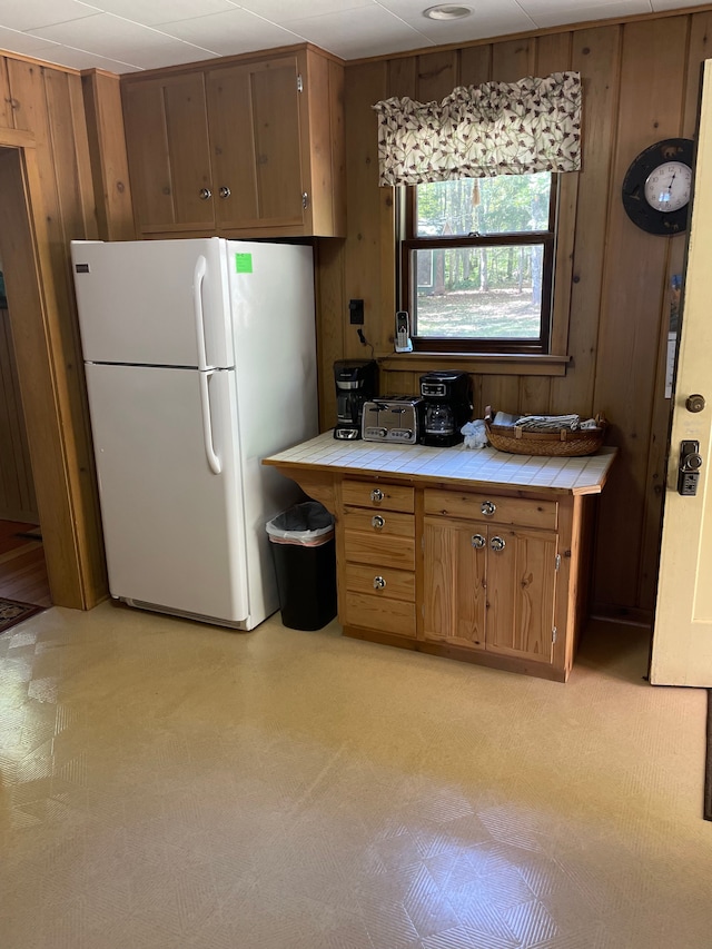 kitchen featuring wood walls, tile counters, and white fridge